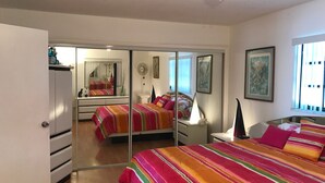 Una camera da letto con un armadio a specchio, un letto con lenzuola colorate, un comodino con una lampada e una finestra con tende.