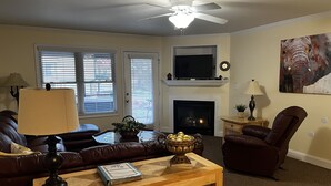 A living room with a fireplace, a ceiling fan, and a television. - Luxury Condo In Town (Helen)