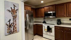 A kitchen with wooden cabinets, stainless steel appliances, and a painting of giraffes and birds on the wall. - Luxury Condo In Town (Helen)