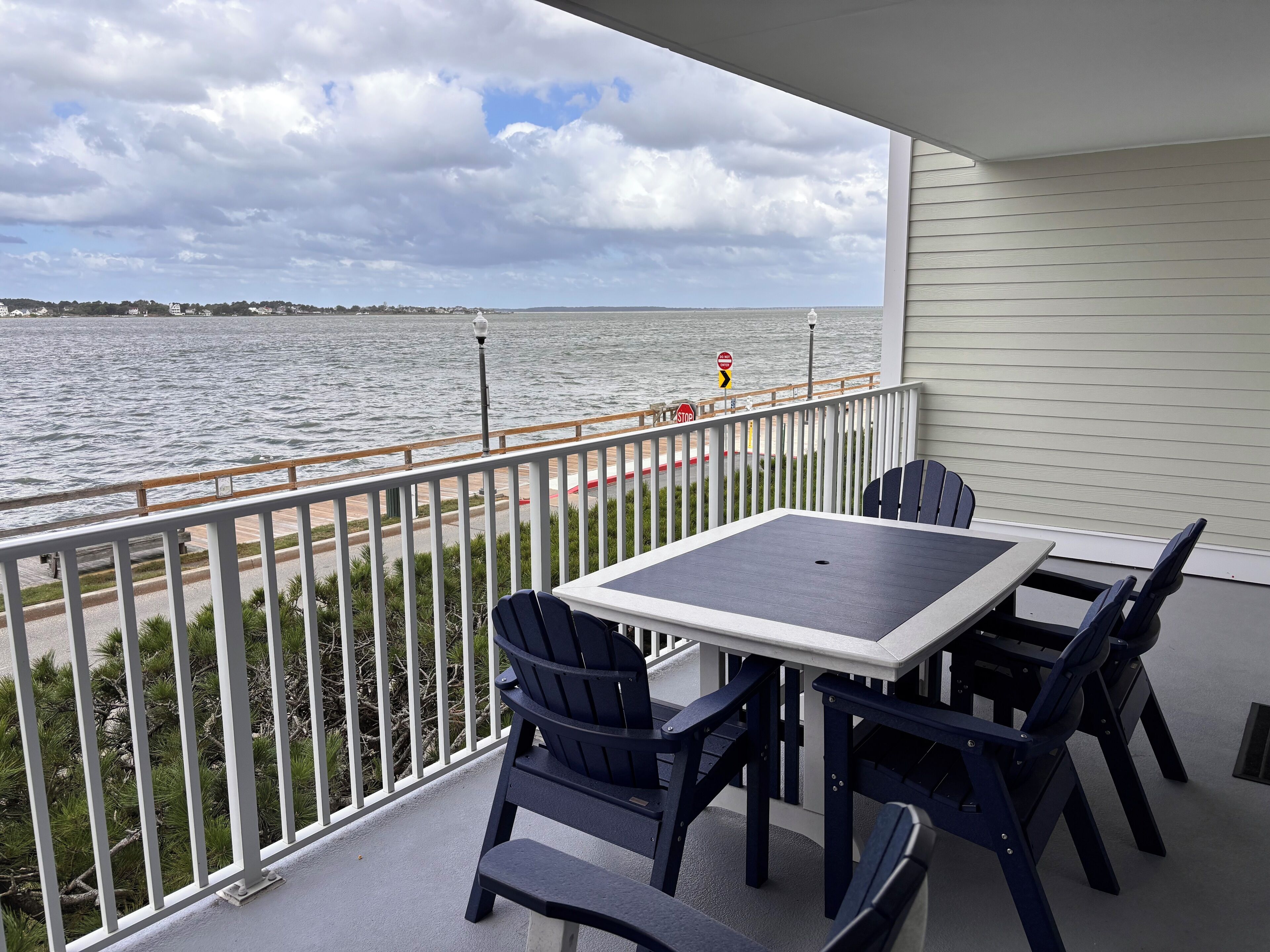 A balcony with a table and chairs, overlooking a body of water and a distant shoreline.