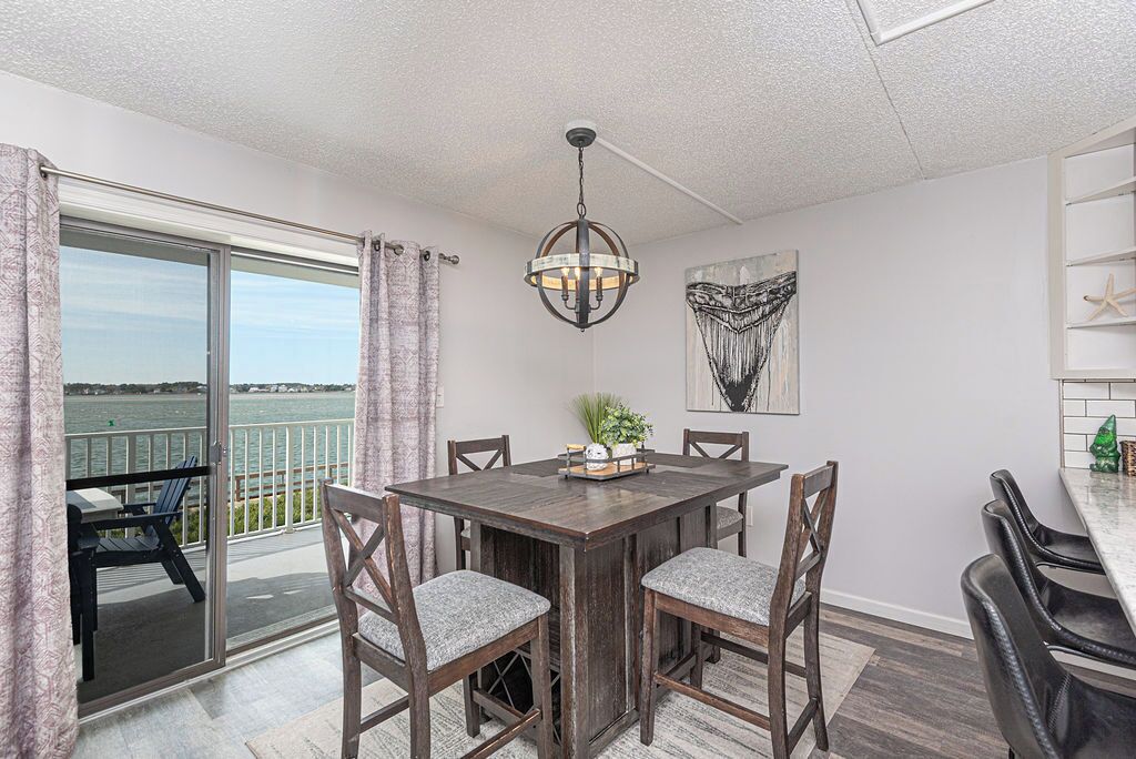 A dining area with a table, chairs, a chandelier, a view of the water, and a painting on the wall.