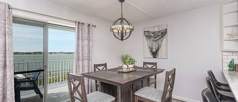 A dining area with a table, chairs, a chandelier, a view of the water, and a painting on the wall.
