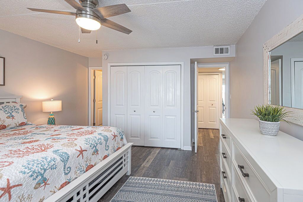 A bedroom with a bed, a ceiling fan, a dresser, a mirror, and a door leading to another room.