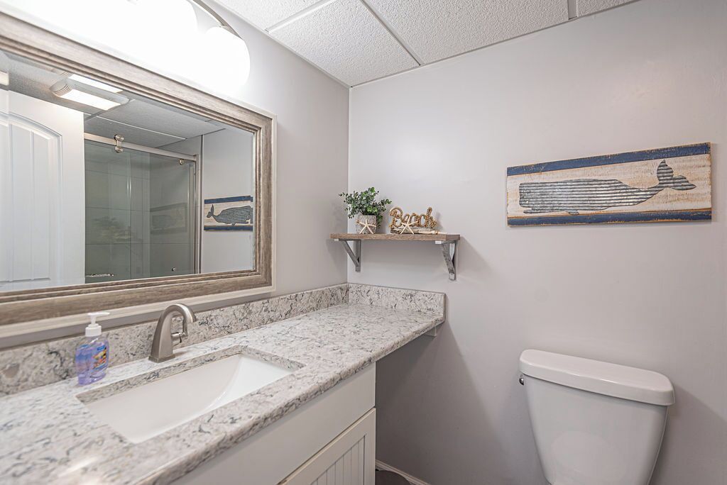 A bathroom with a marble sink, a toilet, a mirror, and a shelf with decorative items.