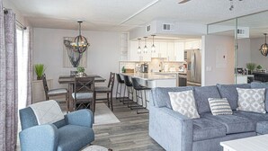 Ein modernes Wohnzimmer mit einer Couch, Sesseln, einem Esstisch und einer Küche im Hintergrund.