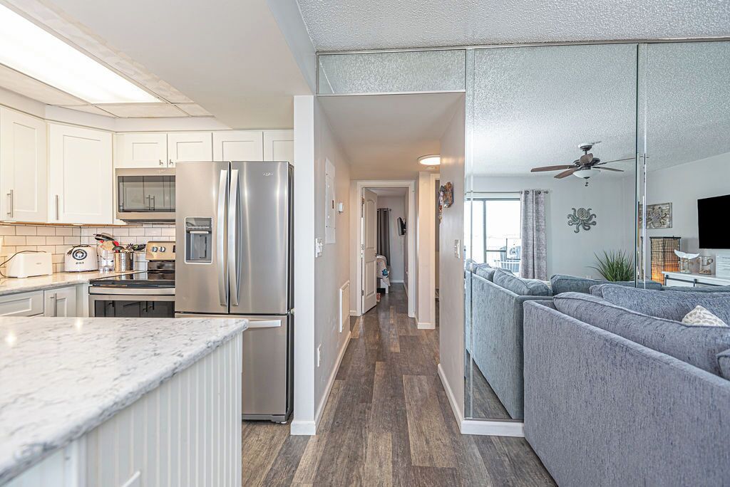 A modern kitchen with white cabinetry, a stainless steel refrigerator, and a marble countertop.