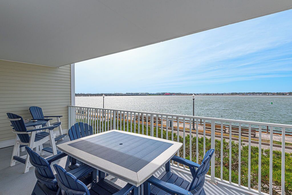 A balcony with a table and chairs, overlooking a body of water and a distant shoreline.