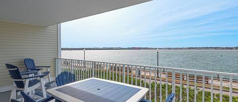 A balcony with a table and chairs, overlooking a body of water and a distant shoreline.