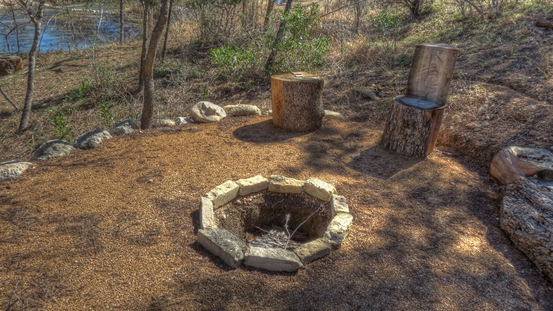 A circular stone fire pit surrounded by a ring of stones, with two wooden stumps nearby.
