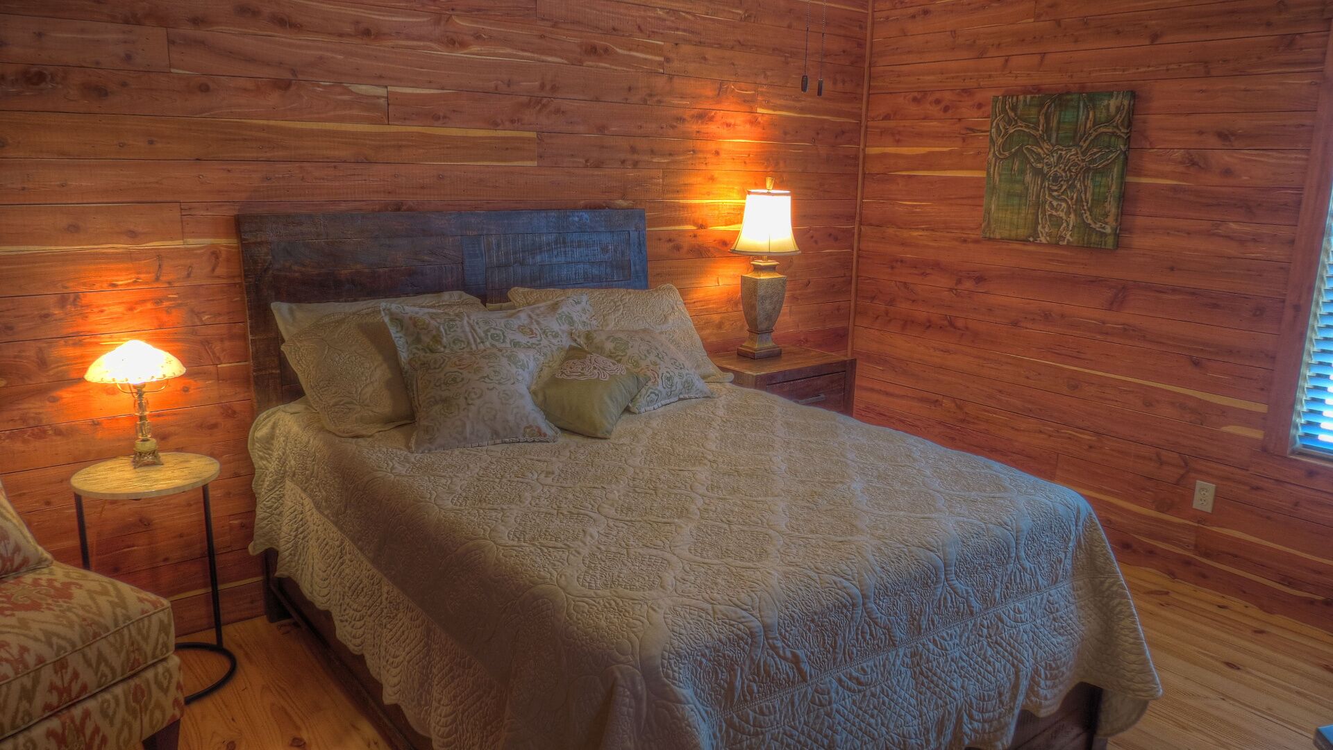 A cozy wooden room with a bed, two bedside lamps, and a decorative wall piece.