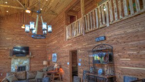 Un interior rústico de madera con una araña, un televisor, una chimenea y un letrero que dice "GOOD FRIENDS".
