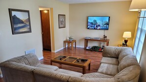 A living room with two beige sofas, a coffee table, a TV mounted on the wall, and a door leading to another room. - Cozy and Spacious Lexington stay (Lexington)