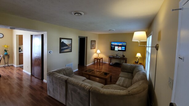 A living room with a sofa, coffee table, and TV. There is a door leading to another room, and a lamp on the wall. - Cozy and Spacious Lexington stay (Lexington)