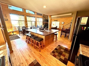 A spacious kitchen with a central island, wooden flooring, and large windows.