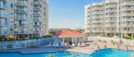 A hotel with a swimming pool, multiple balconies, and a covered seating area.