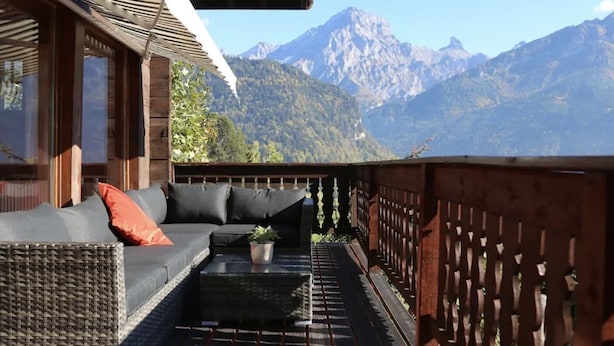 A balcony with a wicker sofa, a small table, and a view of mountains.