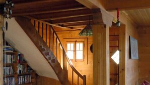 A wooden interior with a staircase, bookshelves, a red rug, and a sofa.