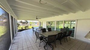 A covered patio area with a table and chairs, large windows, and a ceiling fan. - Sleeps 10 - Available Year Round -  Huge Private Home (Sanibel)