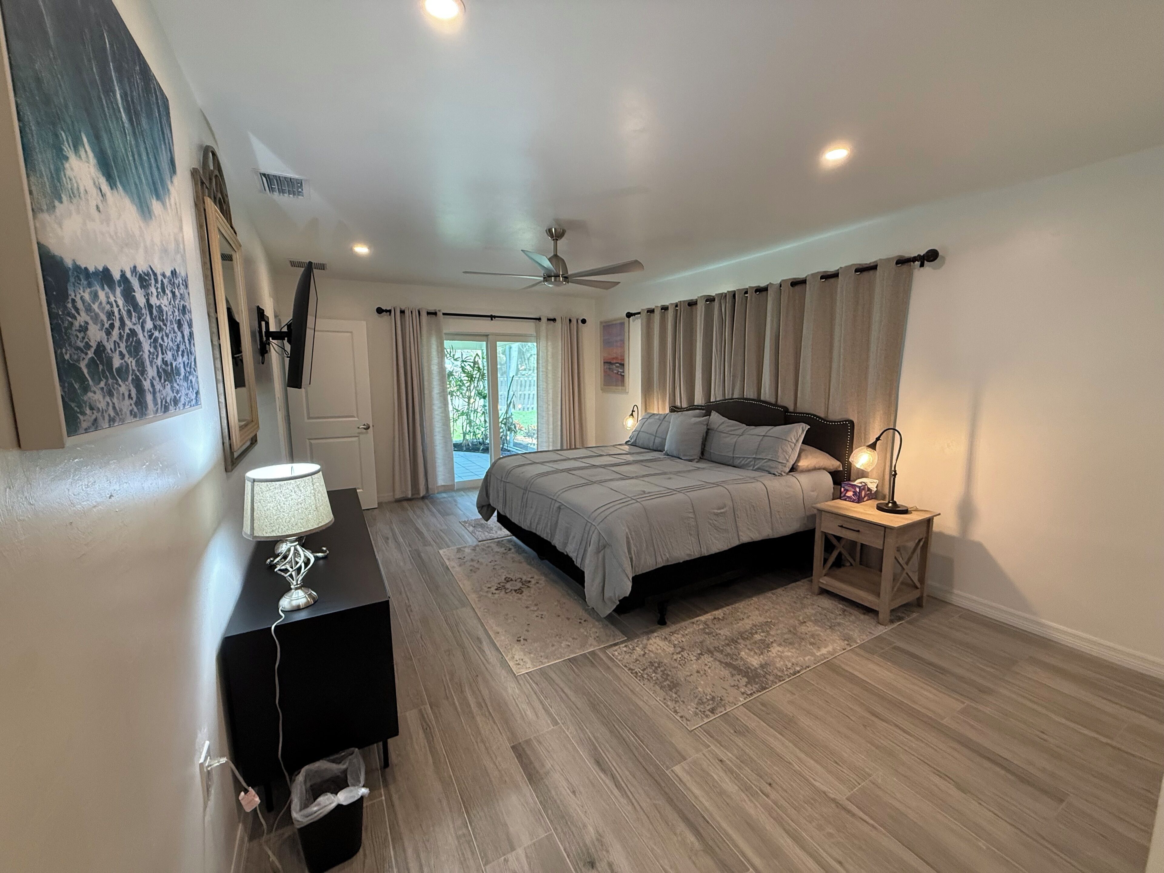 A bedroom with a bed, bedside tables, a desk, a ceiling fan, and a view of the outdoors.