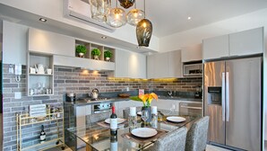 A modern kitchen with a glass dining table, stainless steel appliances, and a brick backsplash. - Modern Mexican 1BR | 2 Pool, Gym & Balcony (Puerto Vallarta)