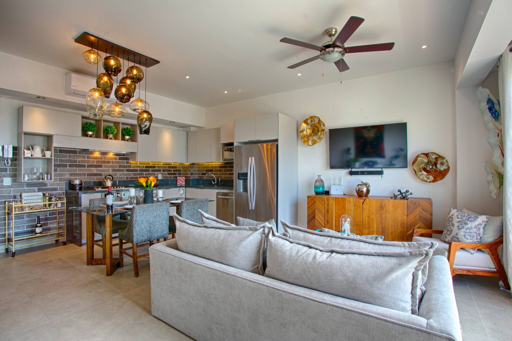 A modern kitchen with a built-in oven, a dining area with a glass table, and a living room with a sofa and a TV.