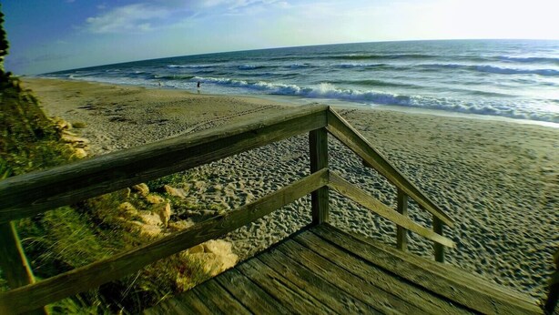 A wooden boardwalk leading to a beach with waves and a clear sky.