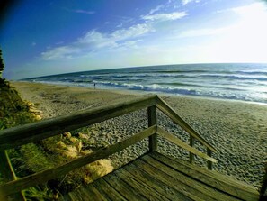 A wooden boardwalk leading to a beach with waves and a clear sky.
