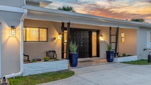 A modern house with a front porch, a black door, and two potted plants.