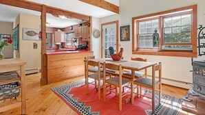 A cozy kitchen with wooden beams, a dining area with a red rug, and a large window with a view of greenery. - Perfect Family home, AC, Heated Pool, 3BR 2Bath (East Hampton)