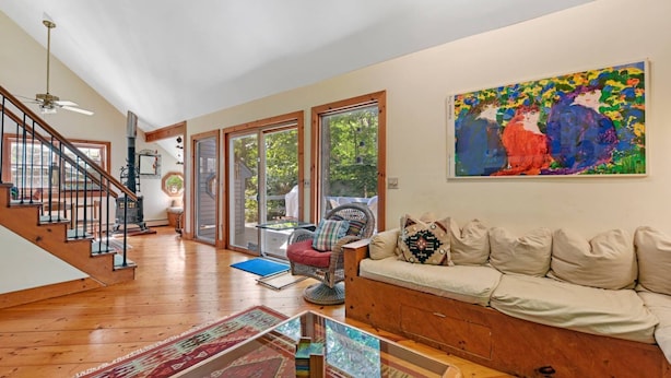 A spacious living room with a wooden staircase, a large window, and a colorful abstract painting. - Perfect Family home, AC, Heated Pool, 3BR 2Bath (East Hampton)