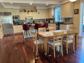 Una cucina moderna con zona pranzo, caratterizzata da frigorifero in acciaio inossidabile, microonde e piano cottura, pavimento in legno e una finestra che offre luce naturale.
