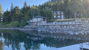 Una propiedad frente al lago con un muelle de madera, un pabellón y una casa grande con muchas ventanas y balcones.