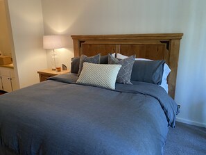 A neatly made bed with a grey bedspread and multiple pillows, a wooden headboard, a bedside table with a lamp, and a nightstand with a candle and decorative items. - Lakefront Gated Brockway Springs Condo (Kings Beach)