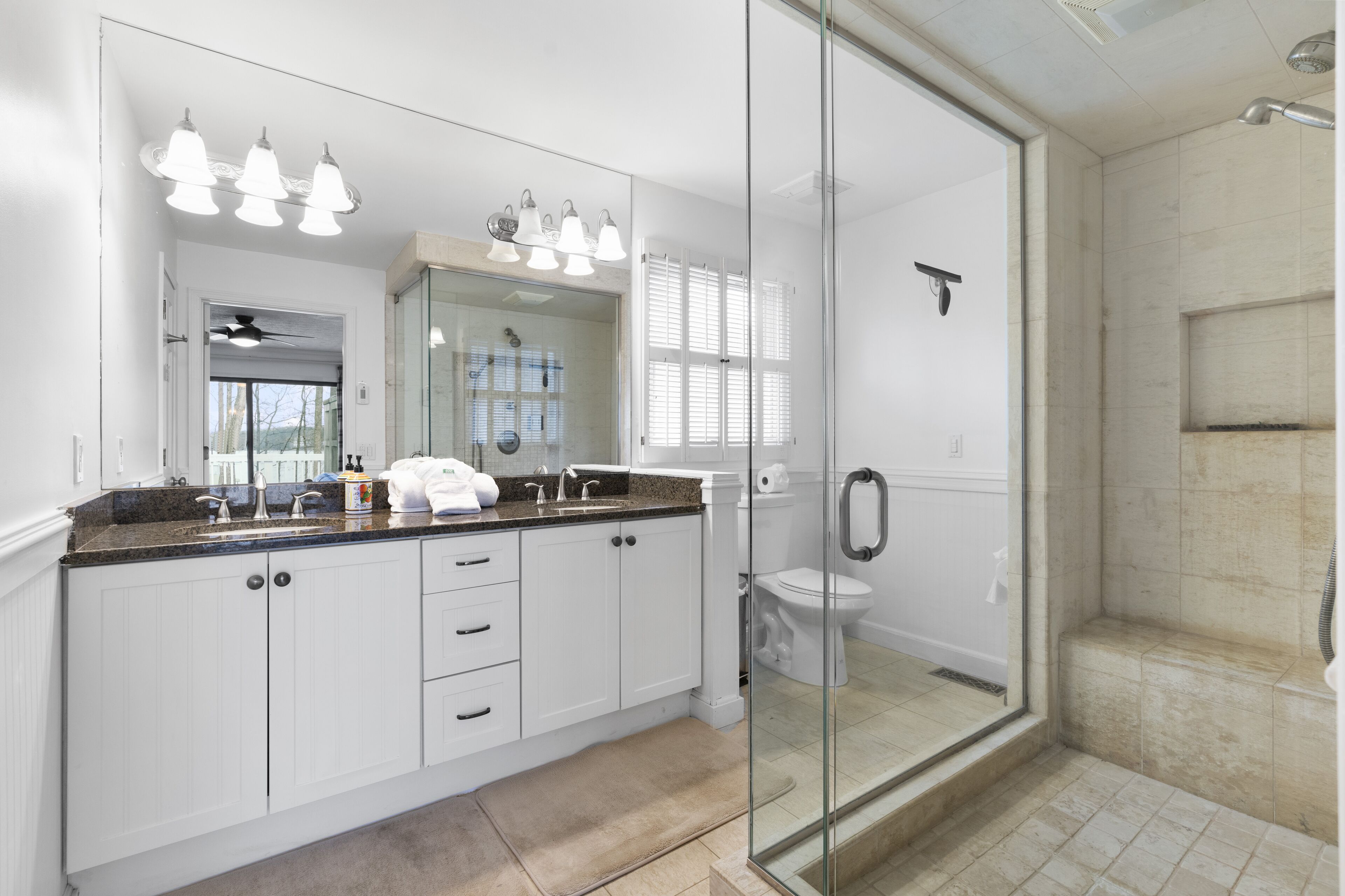 A modern bathroom with a glass-enclosed shower, white cabinetry, and a large mirror with pendant lighting.