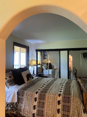 A bedroom with an arched ceiling, a bed with patterned bedding, bedside lamps, and a mirror.