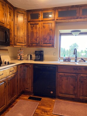 A kitchen with wooden cabinets, a dishwasher, a coffee maker, and a window with a view of trees.