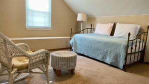 Une chambre à coucher avec un lit, un fauteuil à bascule et un petit pouf.