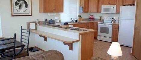 A compact kitchen with wooden cabinets, a built-in island, a microwave, and a stove.