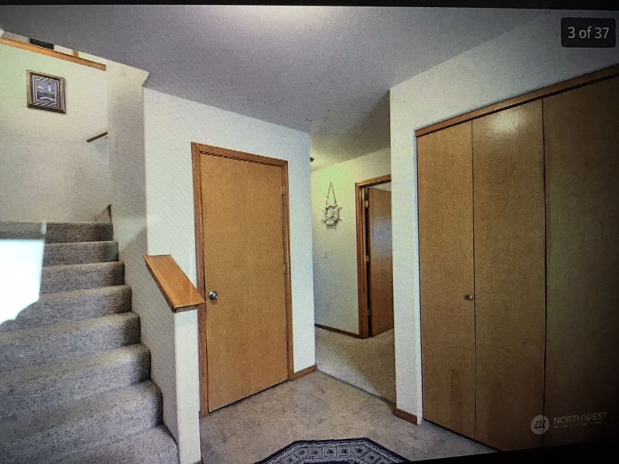 A room with a staircase, a wooden door, a closet, and a small window.