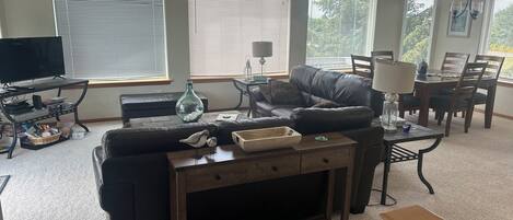 A living room with a sofa, a coffee table, a TV stand, and a dining area with chairs and a table.