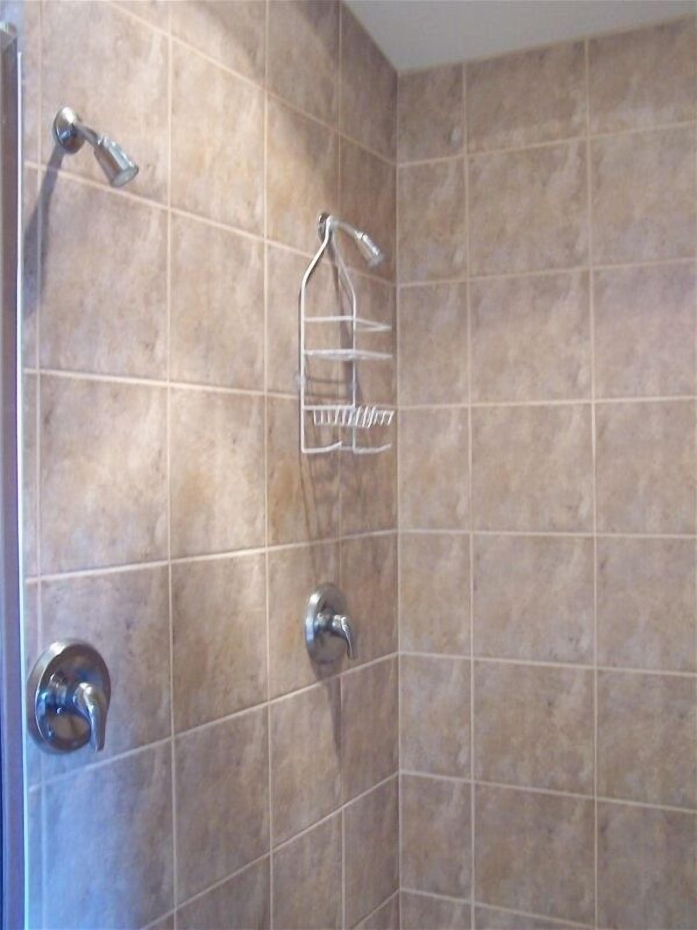 A bathroom with beige tiles, a shower with a handheld showerhead, a towel rack, and a toilet with a round flush handle.