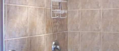 A bathroom with beige tiles, a shower with a handheld showerhead, a towel rack, and a toilet with a round flush handle.