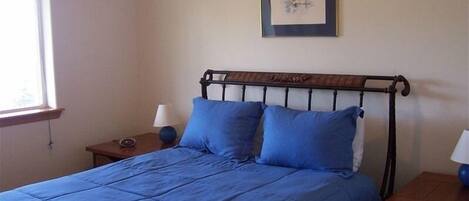 A bedroom with a bed, a nightstand, a lamp, and a framed picture on the wall.