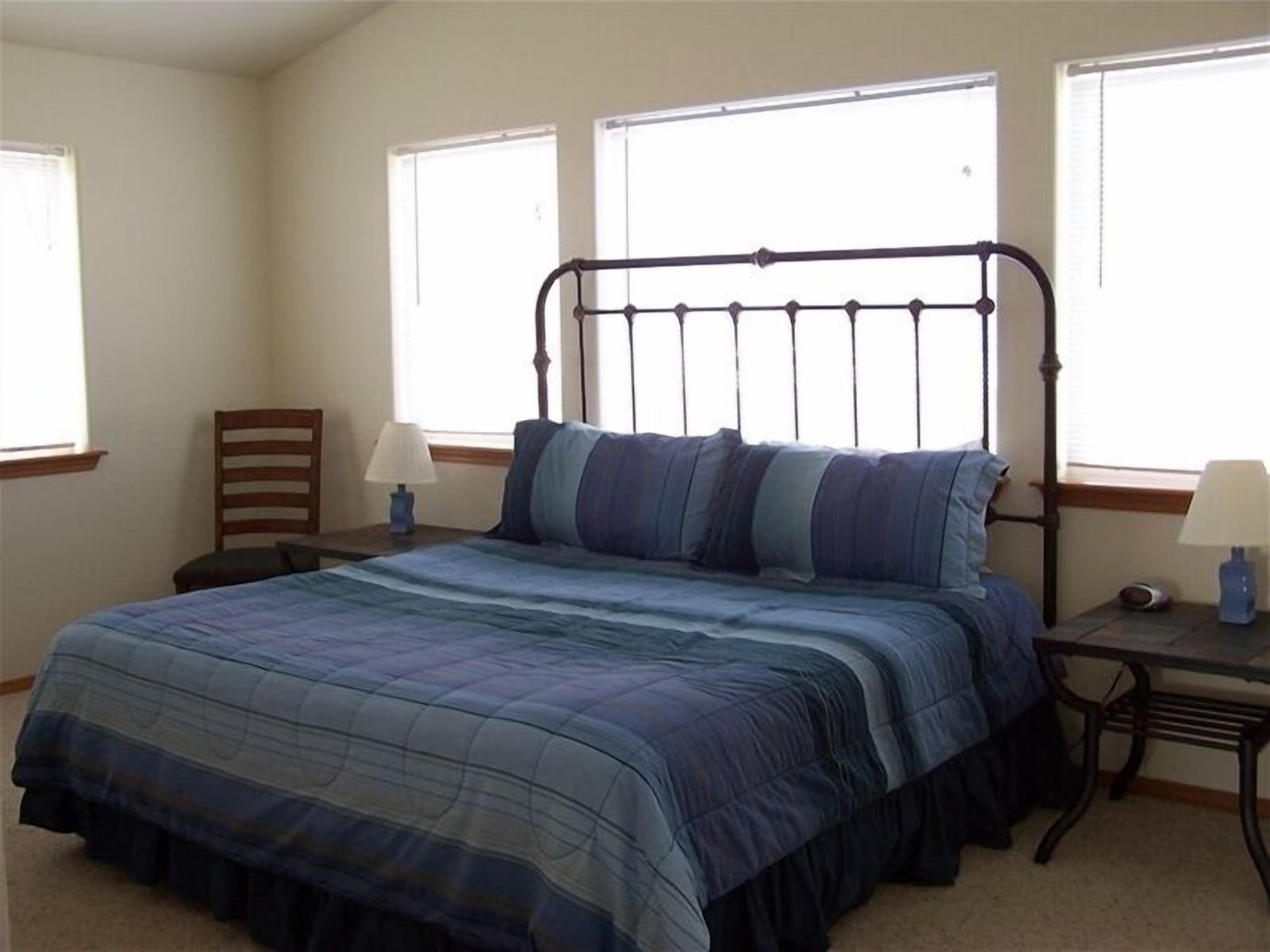 Una camera da letto con un letto, due comodini, una sedia e tre finestre.