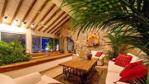 Un salon chaleureux avec un mur en pierre, une table basse en bois et un canapé agrémenté de coussins rouges.