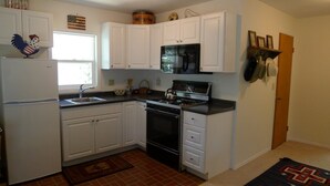 A compact kitchen with white cabinets, a stove, a microwave, and a refrigerator. - Located on the Historic Gunnison River-Casa Del Rio (Gunnison)