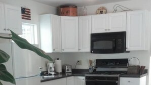 A compact kitchen with white cabinets, a microwave, a stove, and a toaster. There is a wooden table and a patterned sofa in the living area. - Located on the Historic Gunnison River-Casa Del Rio (Gunnison)