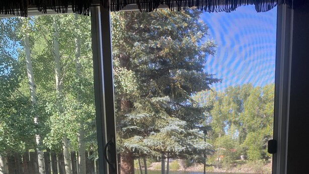 A room with a large sliding glass door leading to an outdoor deck with a bench and a view of a wooded area. - Located on the Historic Gunnison River-Casa Del Rio (Gunnison)