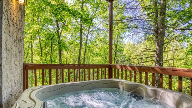 Een hottub met een houten terras en uitzicht op een bos.