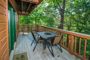 A wooden deck with a table and chairs, surrounded by a wooden railing, overlooking a forested area.